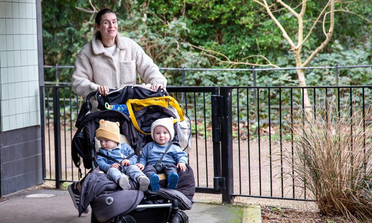 A woman pushes a twin pushchair with twin toddlers sitting in it