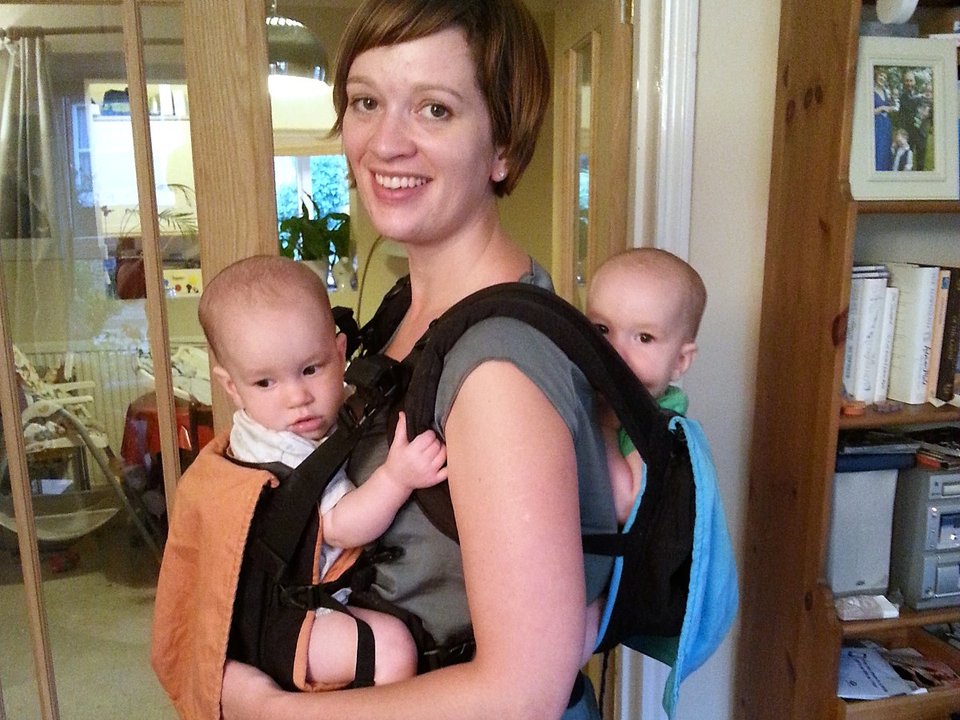 a woman carrying her twins babies with two baby carriers, one on her front and one on her back