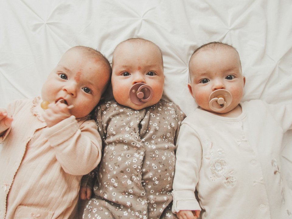 triplet babies lying on a bed with dummies in their mouths
