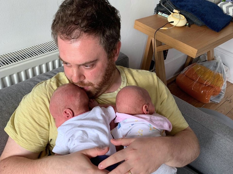 a man sat on a sofa holding twin babies