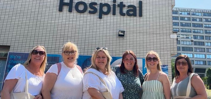 Six women stand together smiling at the camera, in front of a sign for St Thomas' Hospital