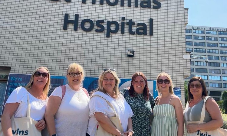 Six women stand together smiling at the camera, in front of a sign for St Thomas' Hospital