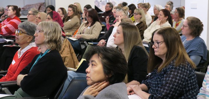 A wide shot of a group of people sitting in a conference room looking towards the front