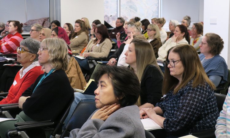A wide shot of a group of people sitting in a conference room looking towards the front