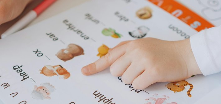 A close up image of a child's hand pointing at a book of basic words and pictures