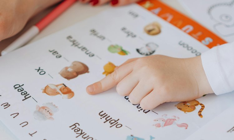 A close up image of a child's hand pointing at a book of basic words and pictures