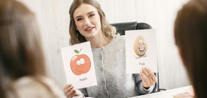 A woman holds up two image cards showing an apple and an egg