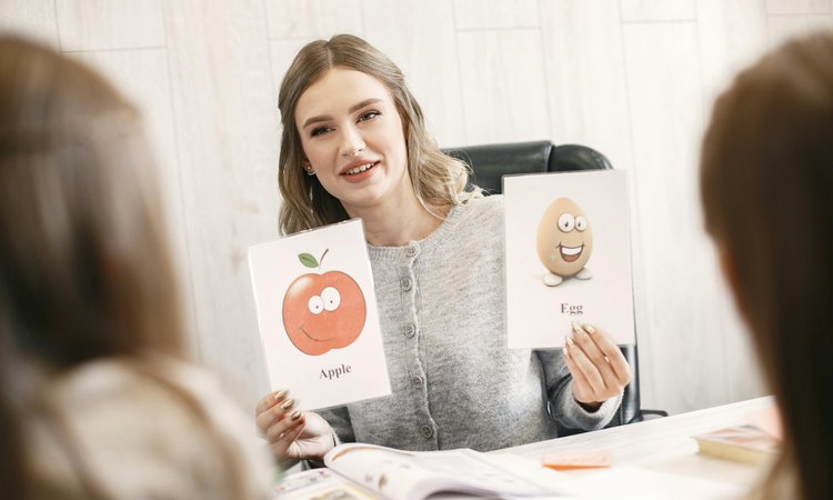 A woman holds up two image cards showing an apple and an egg