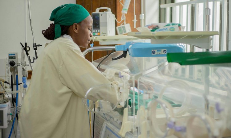 A nurse dressed in scrubs attending to a neonatal crib