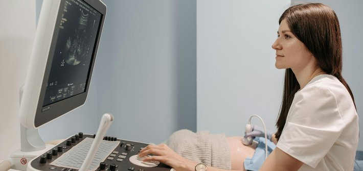 A side view of a sonographer sitting at an ultrasound machine