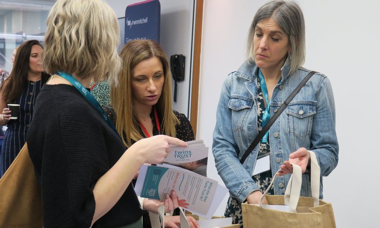 Three women stand together looking at handouts