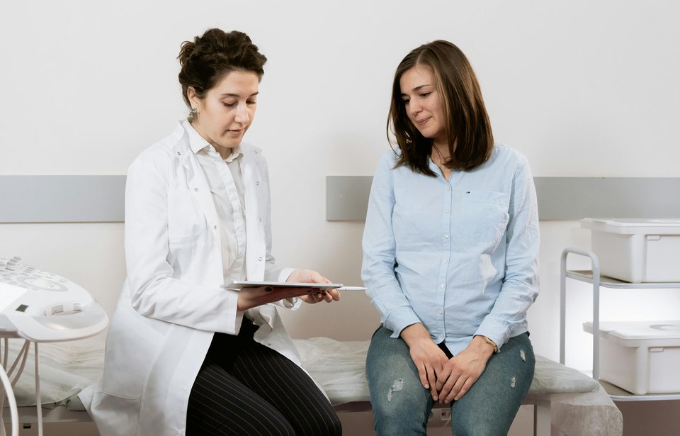 Two women sit on a hospital bed as one explains something to the other using a tablet