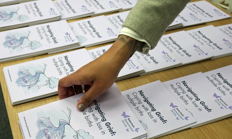 A close up of a hand reaching to pick a booklet off a table
