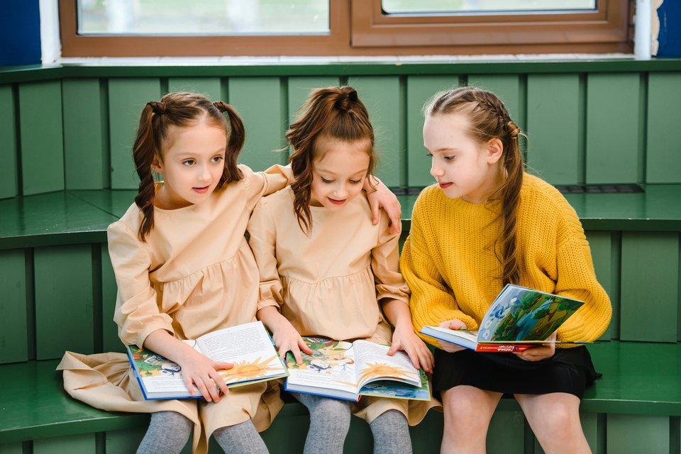 Three young girls sit together reading books