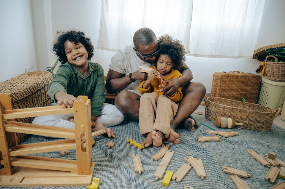 A father and twins sit on the floor with building blocks scattered around them