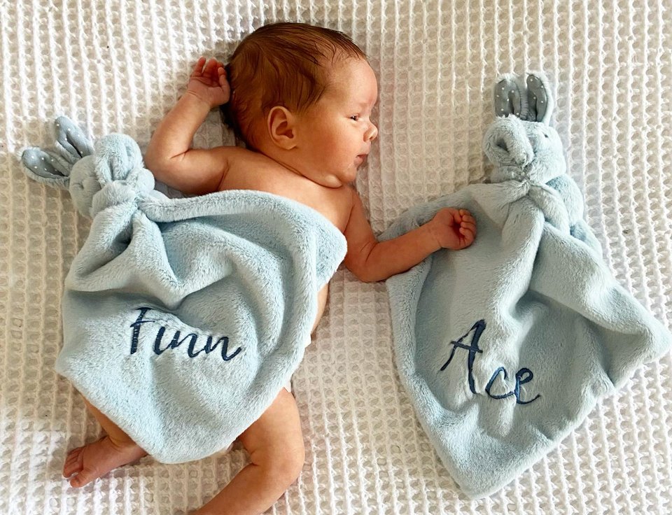 A baby lies under a blue towel with another towel next to them