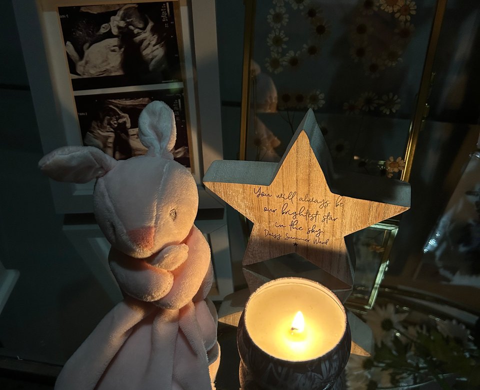 A lit candle in front of a star, a teddy and a framed photo of a pregnancy scan