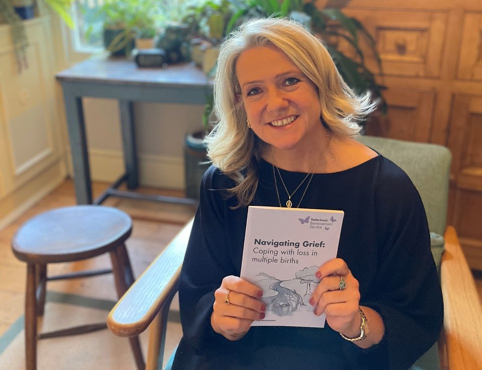 A woman sits smiling at the camera holding a Navigating Grief booklet