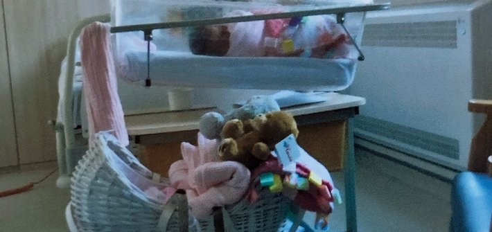 An empty cot is pictured in front of a maternity cot in a hospital room