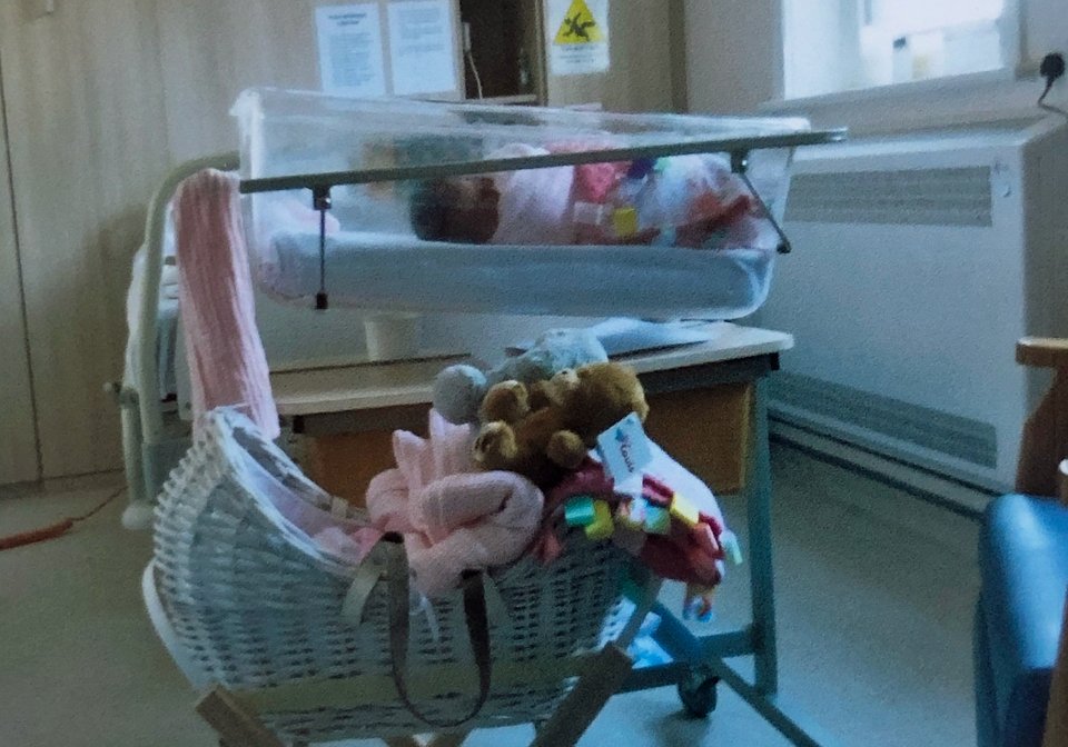 An empty cot is pictured in front of a maternity cot in a hospital room