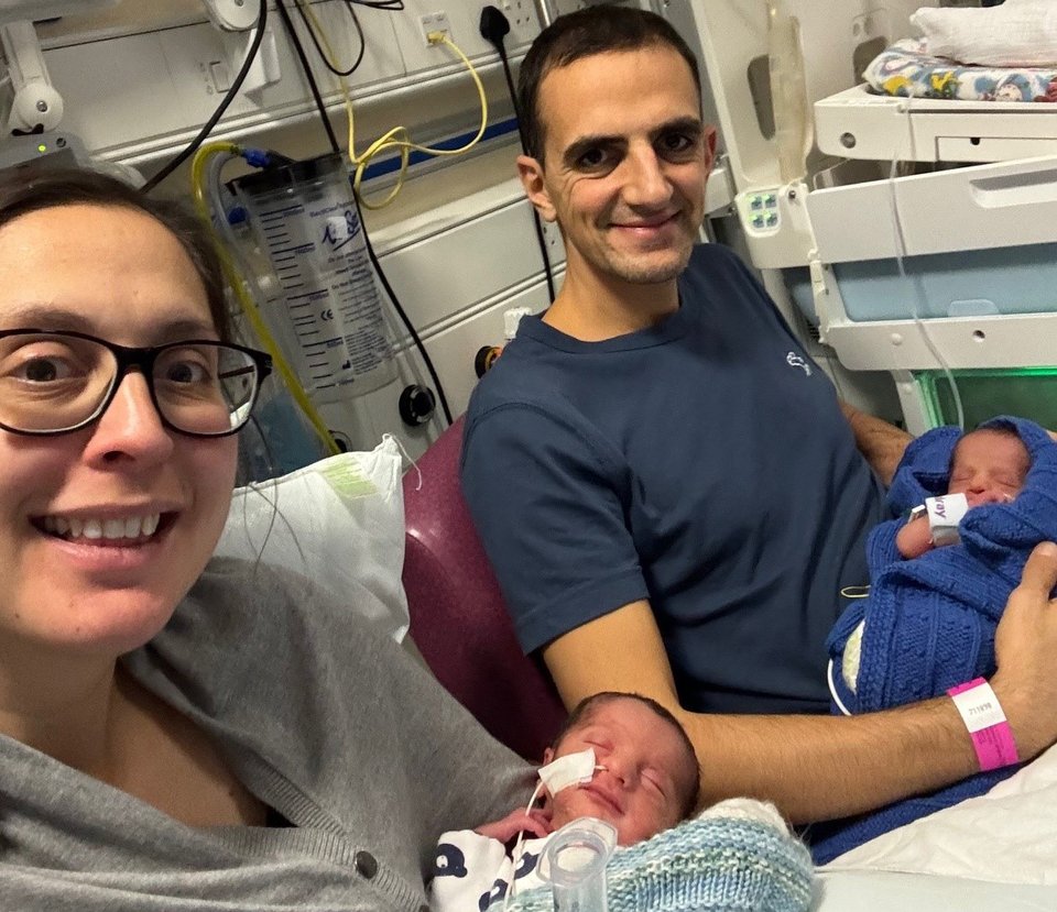 A man and woman sit together in hospital each holding a baby
