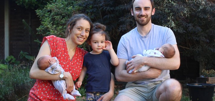 A man and woman each hold a baby with a small girl standing between them
