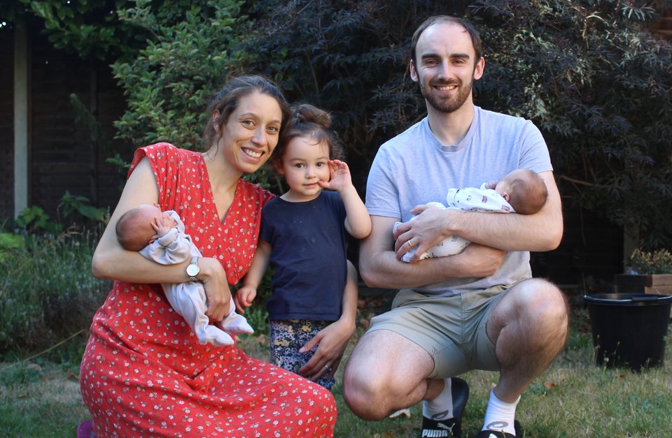 A man and woman each hold a baby with a small girl standing between them