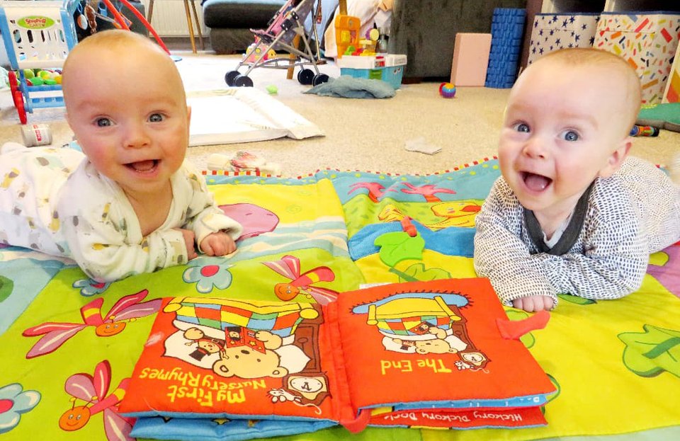Twins lie on the floor looking up smiling at the camera