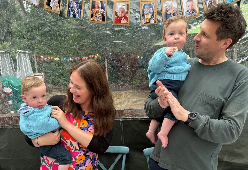 A man and woman stand each holding a baby