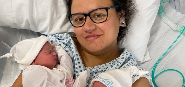 A woman in a hospital gown lies on a bed holding two babies