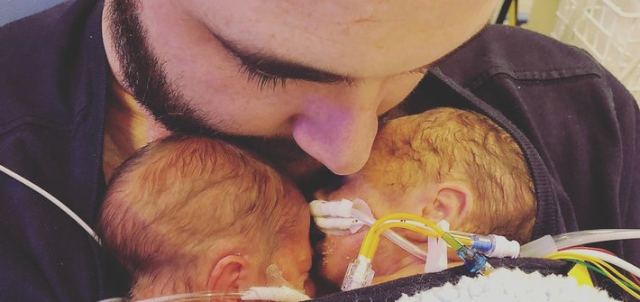 A close up of a man's head dipped towards two premature babies held to his chest