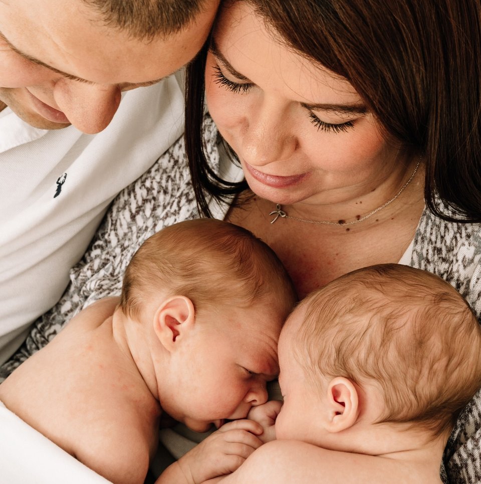 A close-up picture of a man and woman cuddling two babies