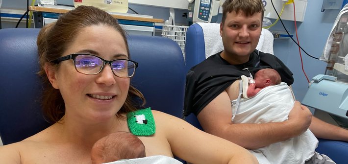 A man and woman sit on hospital chairs each with a baby on their chest
