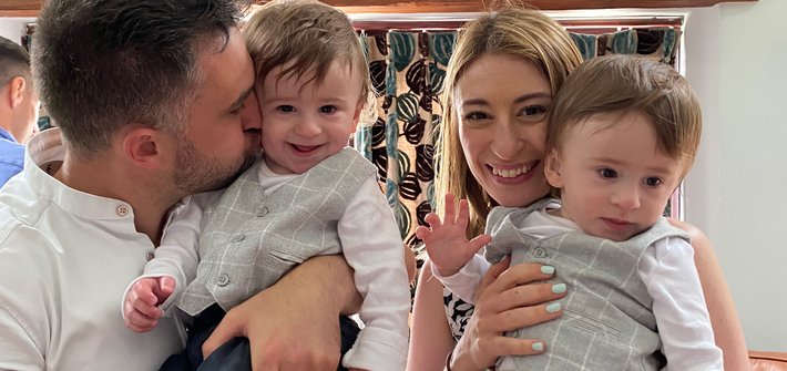 A man and woman stand together each holding a toddler