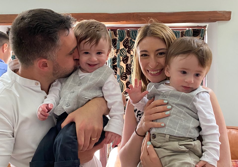 A man and woman stand together each holding a toddler