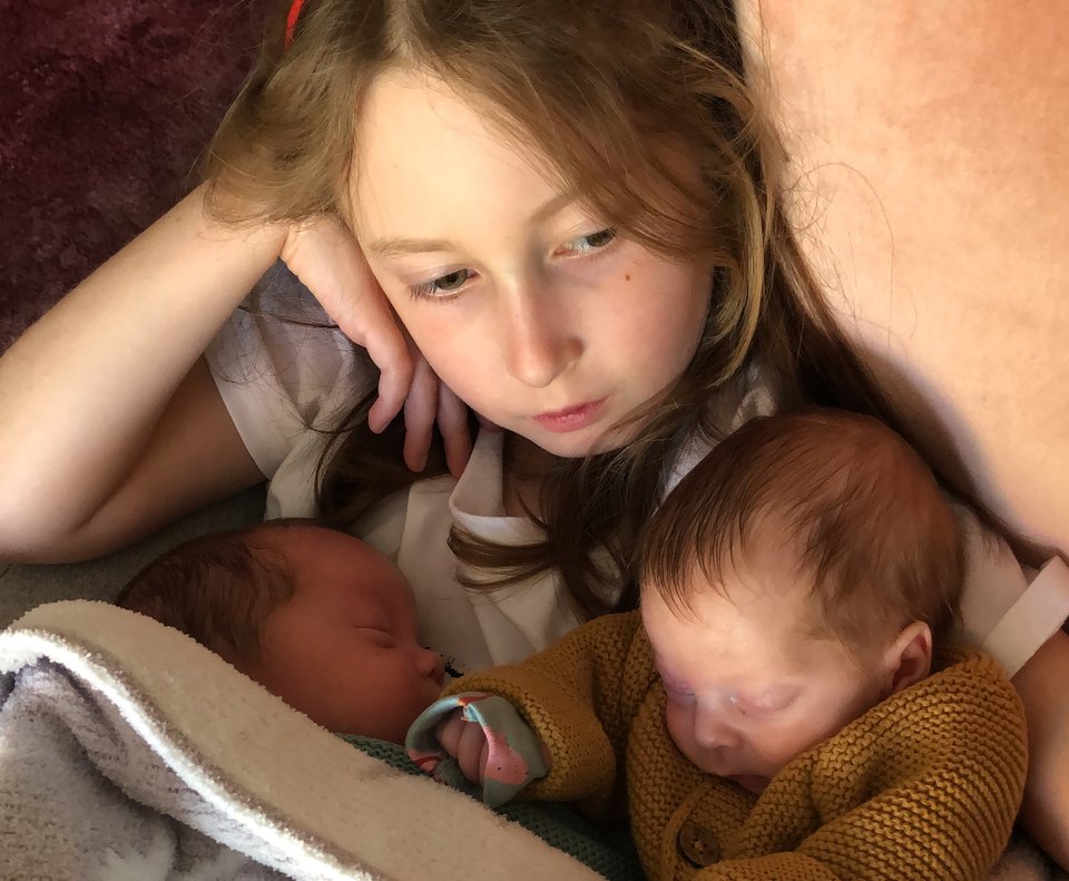 A young girl lies on a sofa cradling twin babies