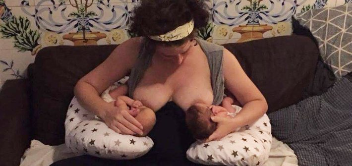 A woman sits on a sofa breastfeeding twin babies