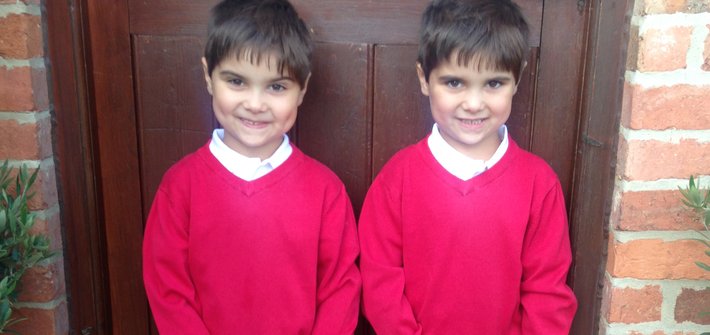 Twin boys in school uniform stand in front of a brown door