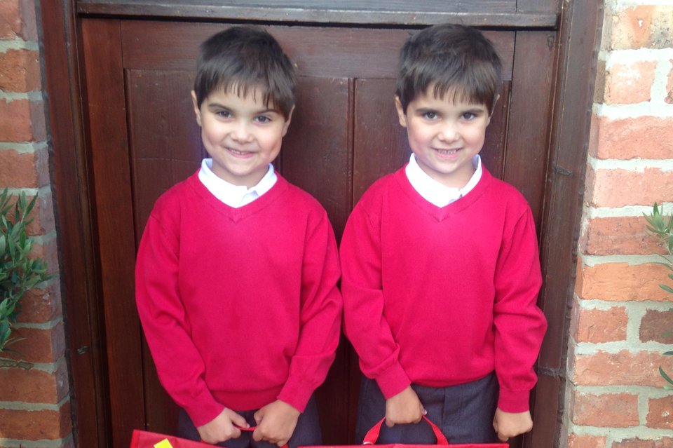 Twin boys in school uniform stand in front of a brown door