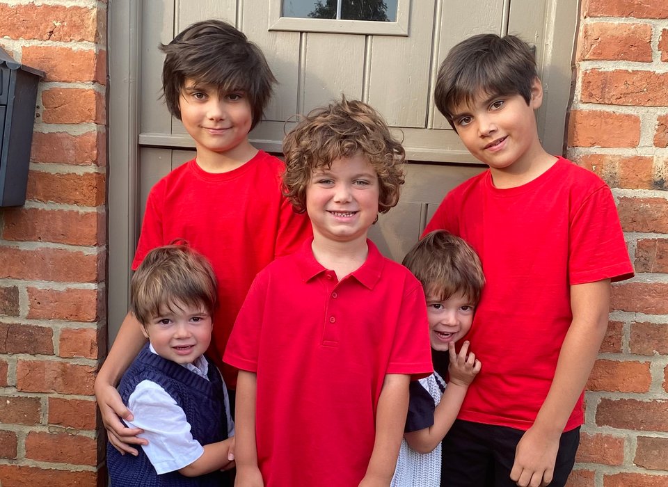 Two sets of twin boys and another boy stand together in front of a grey door
