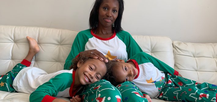 A woman sits on a sofa with twin girls in her lap