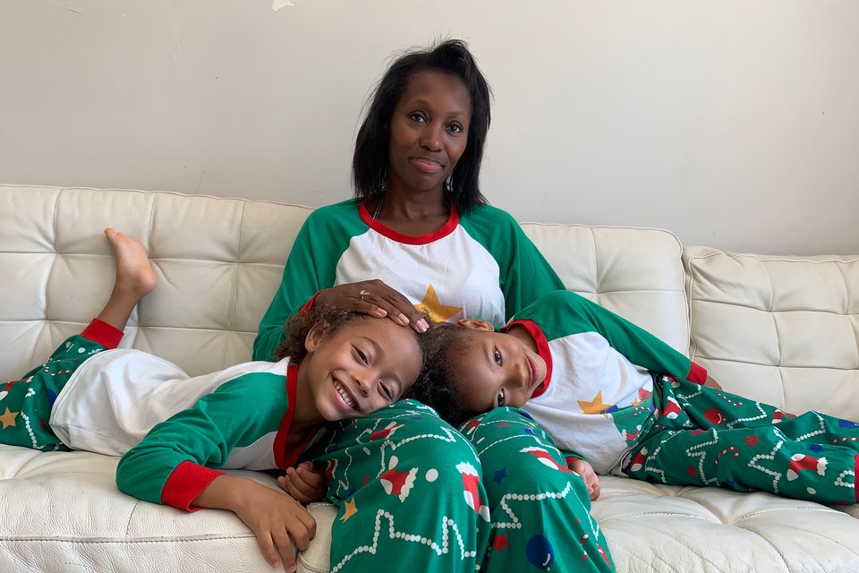 A woman sits on a sofa with twin girls in her lap