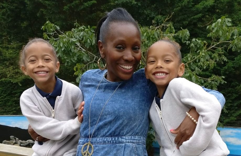 A woman and twin girls with their arms around each other