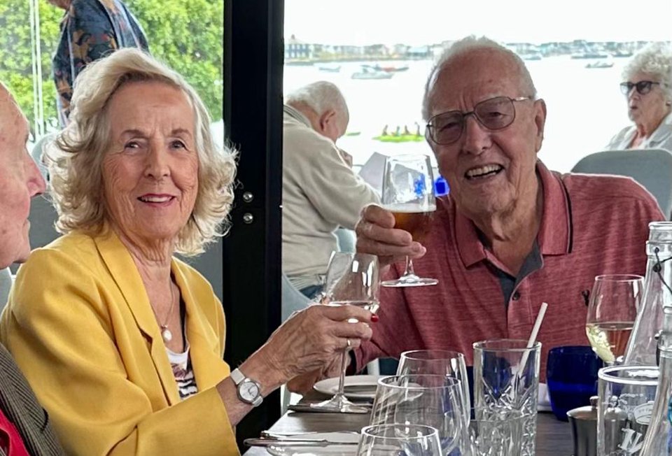 An elderly man and woman sit at a dinner table toasting
