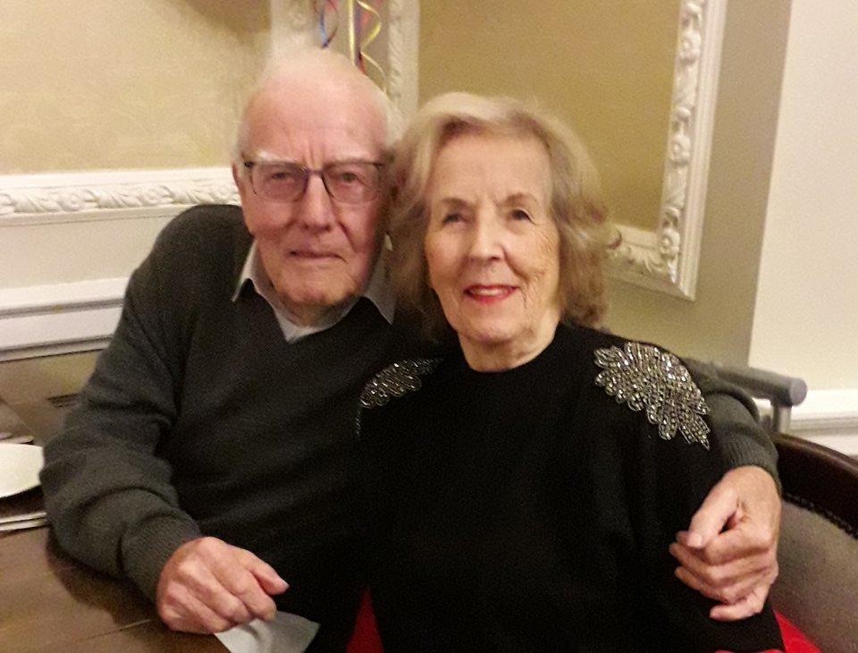 An elderly man and woman with their arms around each other