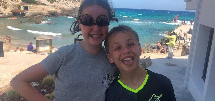 A girl and a boy with their arms around each other in front of a beach