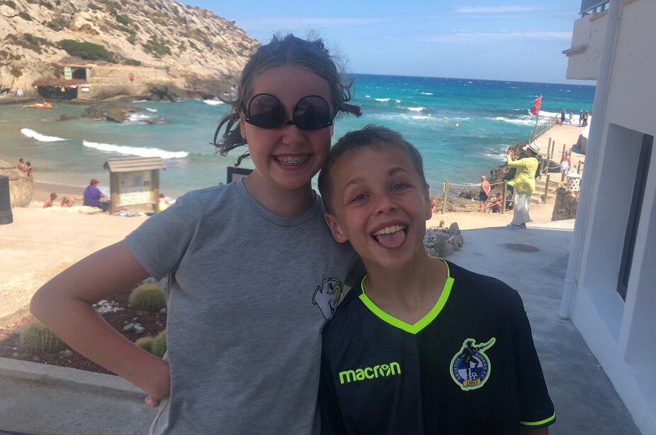 A girl and a boy with their arms around each other in front of a beach