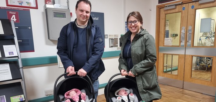 A man and a woman each hold a baby carrier as they prepare to leave hospital