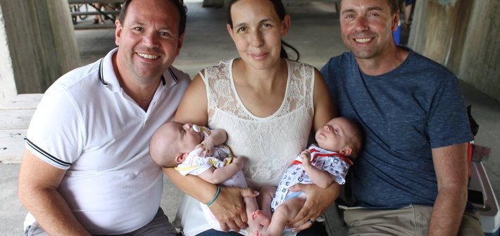 Two men sit either side of a woman who is holding twin babies