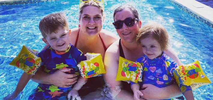 Parents sit in a swimming pool with their twin children